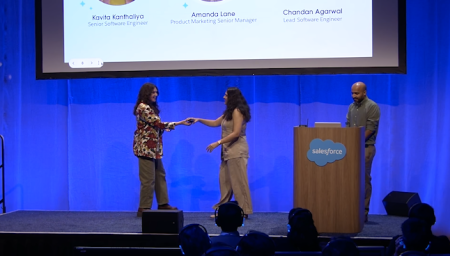 Three presenters on stage, two of them are shaking hands