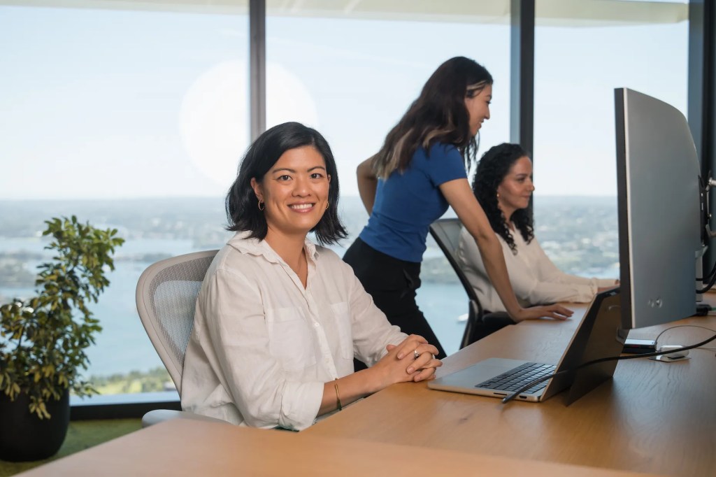 モダンなオフィスで座り、カメラに向かって微笑んでいる白いブラウスを着た女性