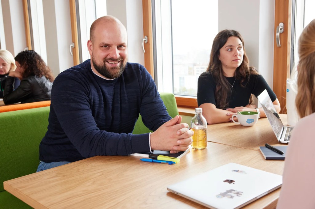モダンなオフィスで一緒に座り、同僚と会話している男性と女性。男性はカメラに向かったポーズを取っています。