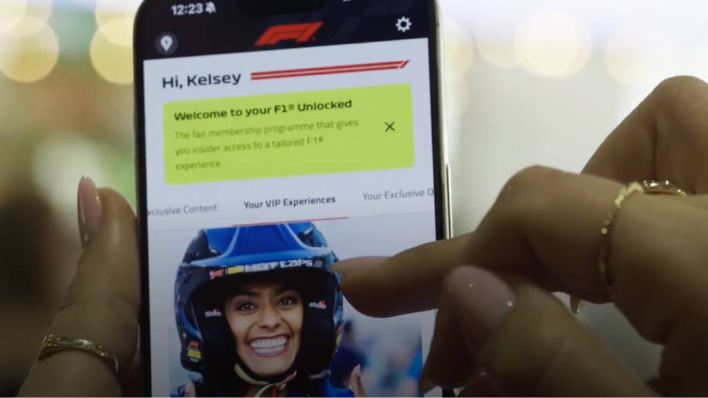 Hands holding a phone showing the F1 app's 'F1 Unlocked' fan membership welcome screen for Kelsey.